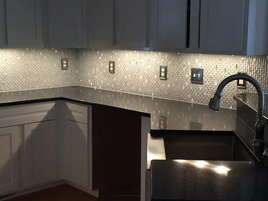 Kitchen counter with dark granite countertop, gray cabinets, mosaic tile backsplash, and a black faucet over the sink, with multiple electrical outlets along the wall.