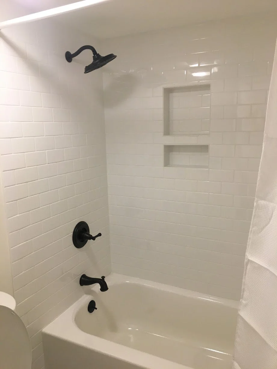 Bathroom shower with white subway tile, black fixtures, a built-in niche, and a bathtub.