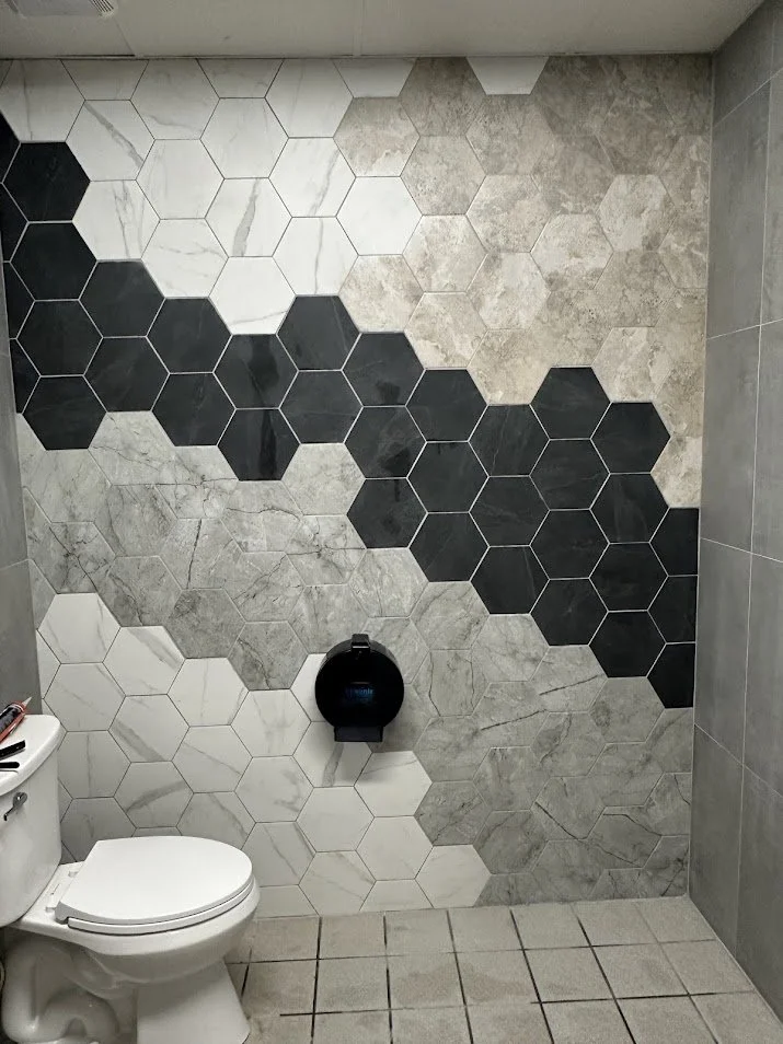 Bathroom with a wall decorated with a hexagon tile pattern in white, black, and gray colors, and a white toilet in the lower left corner.