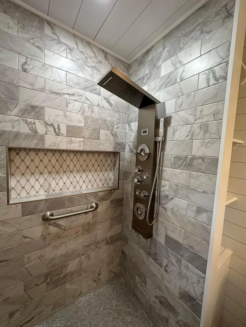 Modern shower with marble tile walls, built-in shelf, and a rainfall showerhead with multiple controls.