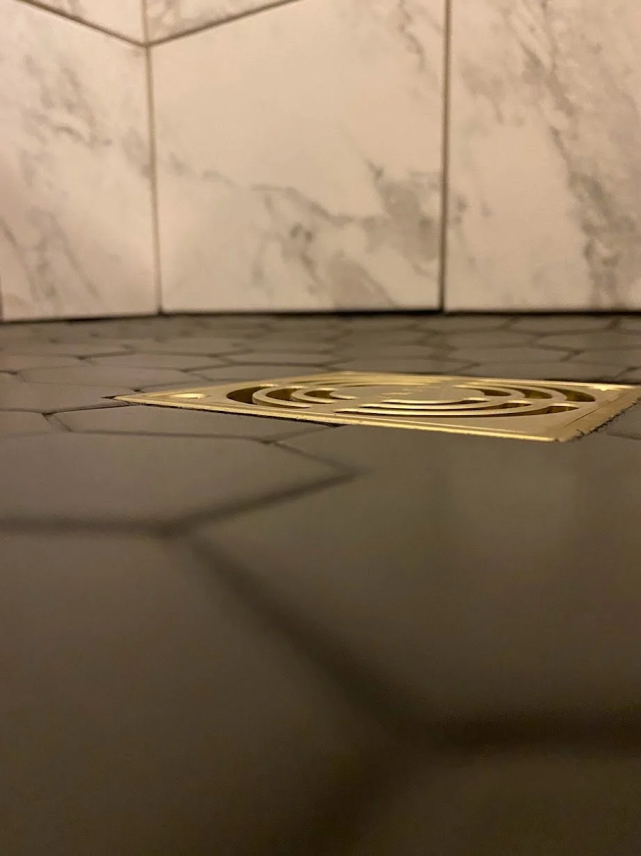 Close-up of a floor drain with a metal grate in a tiled bathroom or shower area.