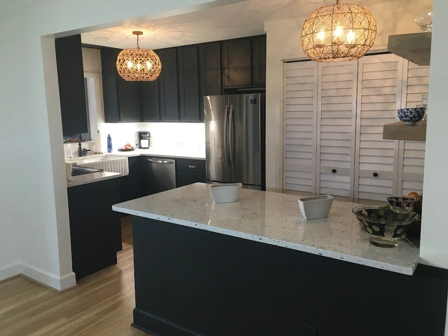 Modern kitchen with black cabinets, stainless steel refrigerator, white speckled countertop island, and two woven pendant lights