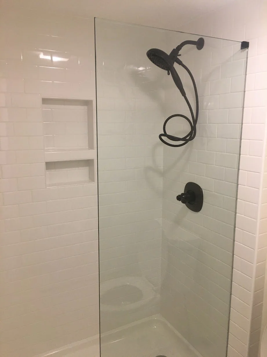 Shower with black handheld showerhead, black control handle, white subway tile walls, and built-in wall niches.
