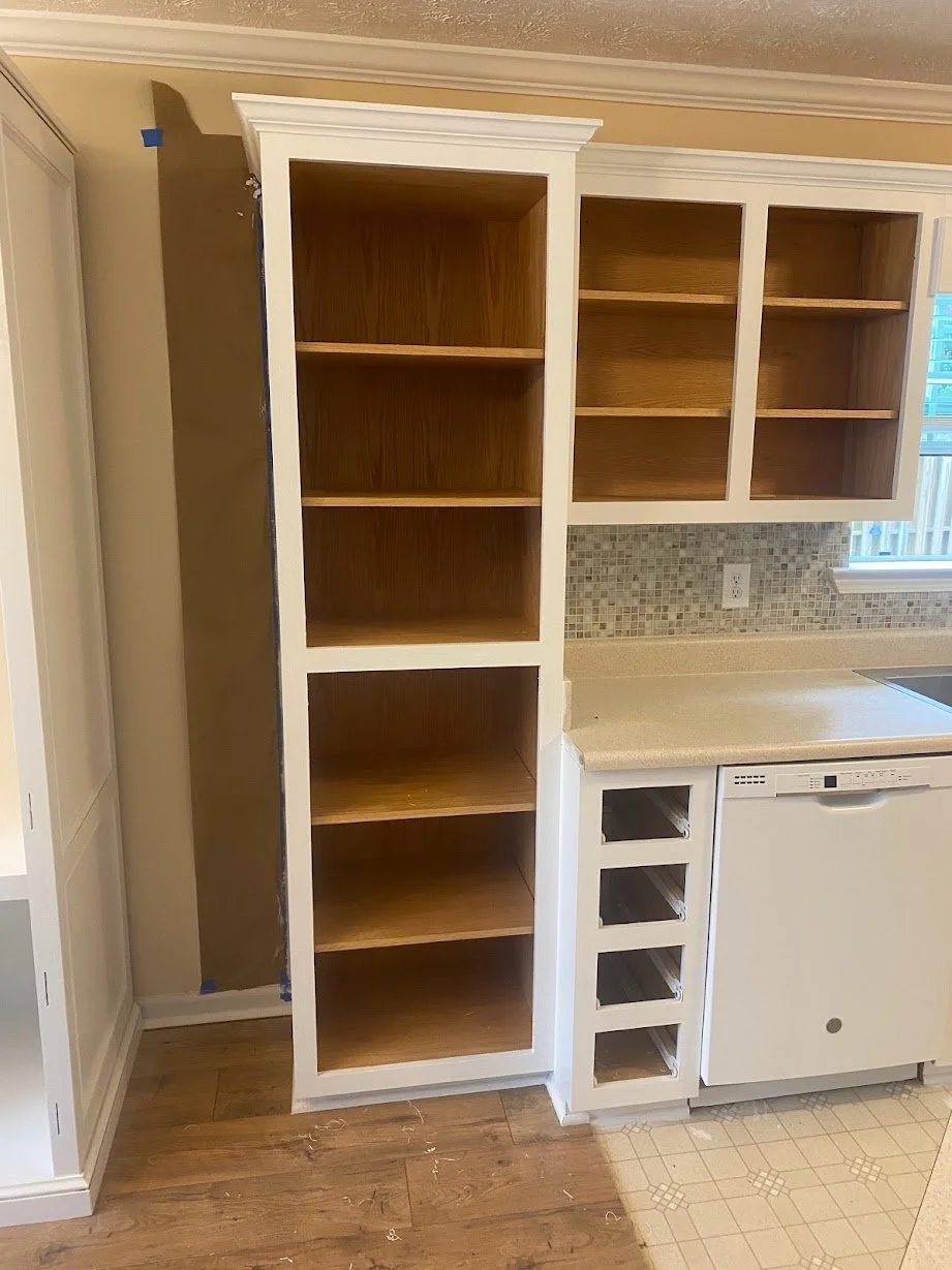 Kitchen with unfinished cabinetry, open shelves, and a tiled backsplash with a window in the background.