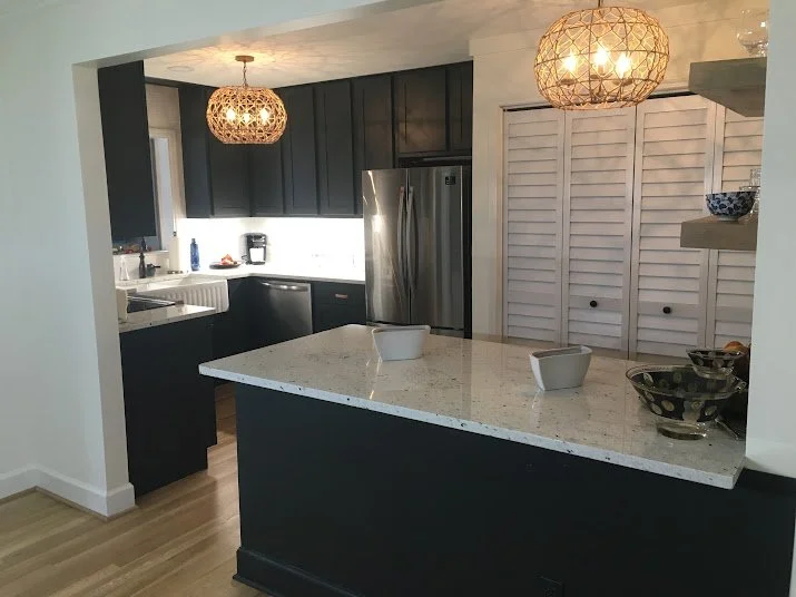 Modern kitchen with black cabinetry, a white speckled island, stainless steel refrigerator, and two woven pendant lights hanging from the ceiling.