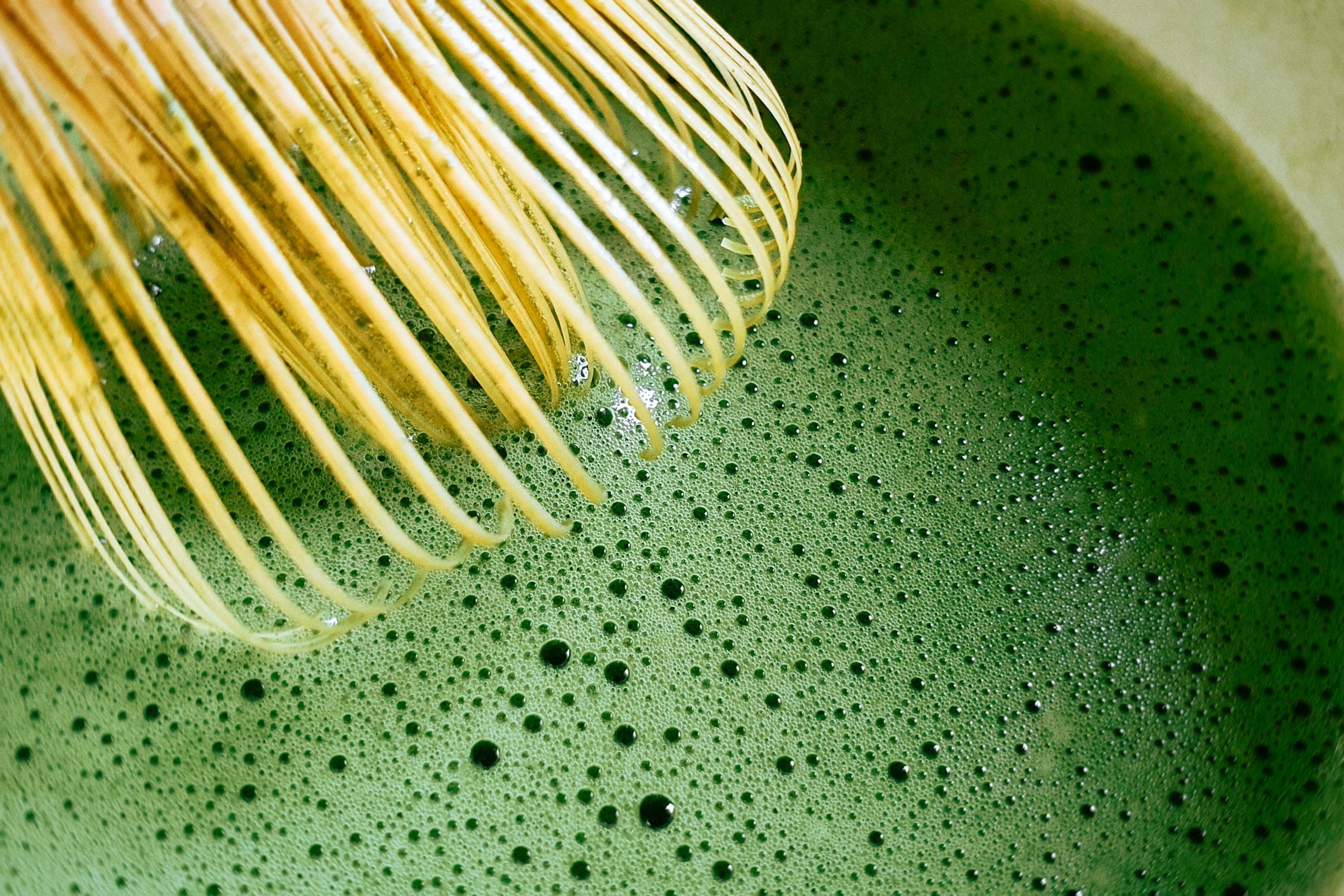 Green matcha tea or batter being whisked with a bamboo whisk.