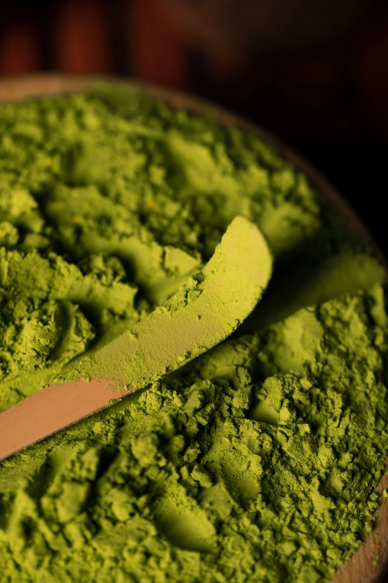 Close-up of bright green matcha powder in a container with a wooden spatula.