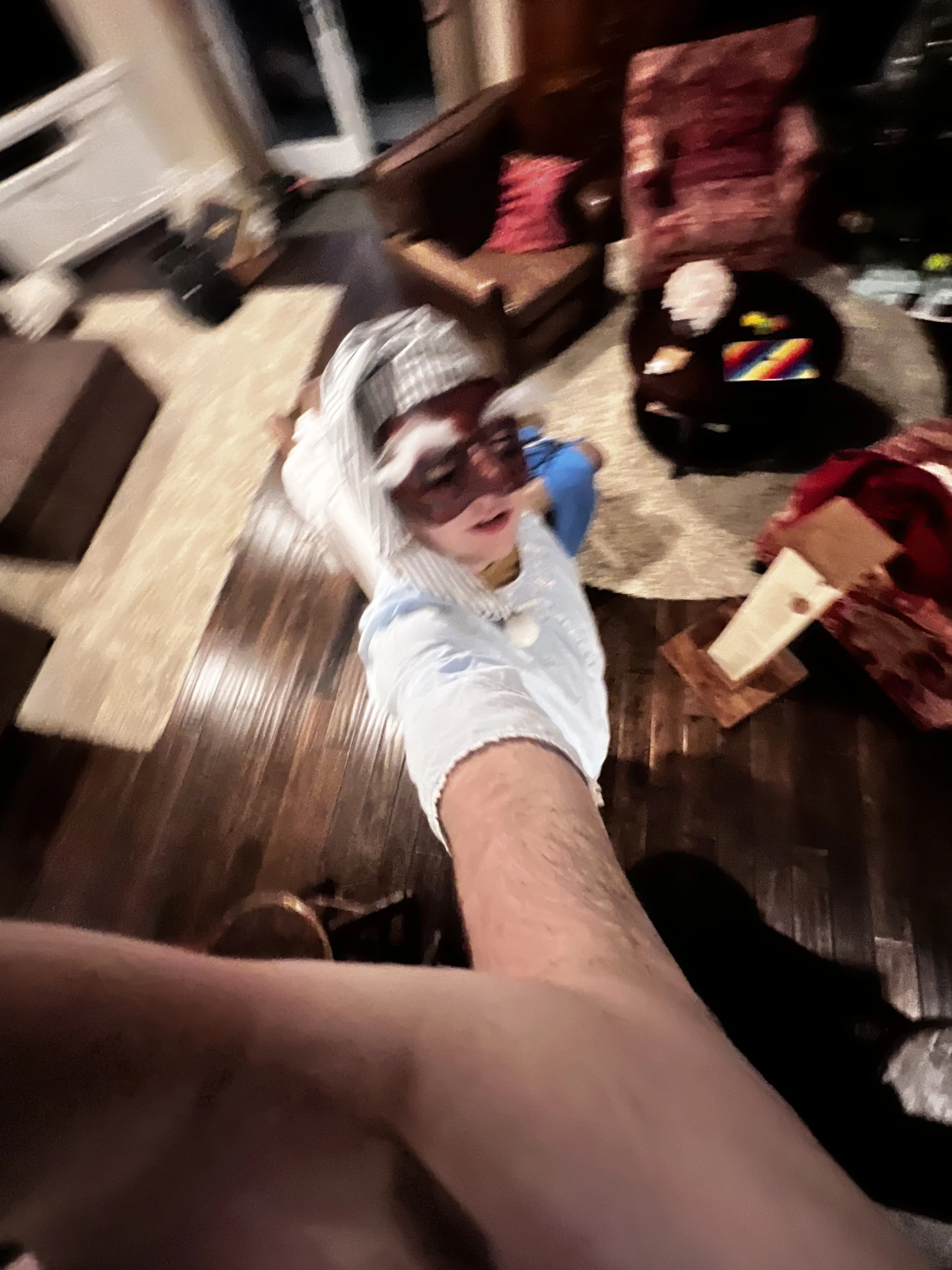 Blurred photo of a person taking a selfie from a high angle, with a child wearing sunglasses and a costume in the background.