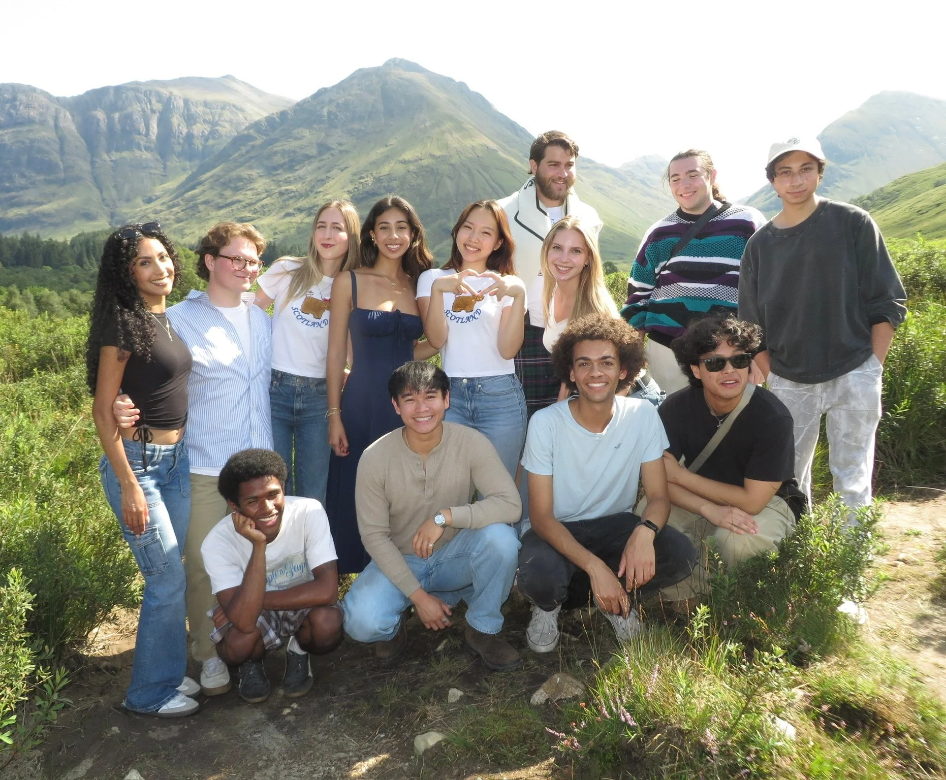 Group of friends smiling outdoors in front of green mountains with blue sky.