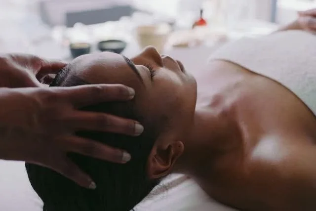 A woman receiving a facial massage or skincare treatment at a spa, lying on her back with eyes closed.
