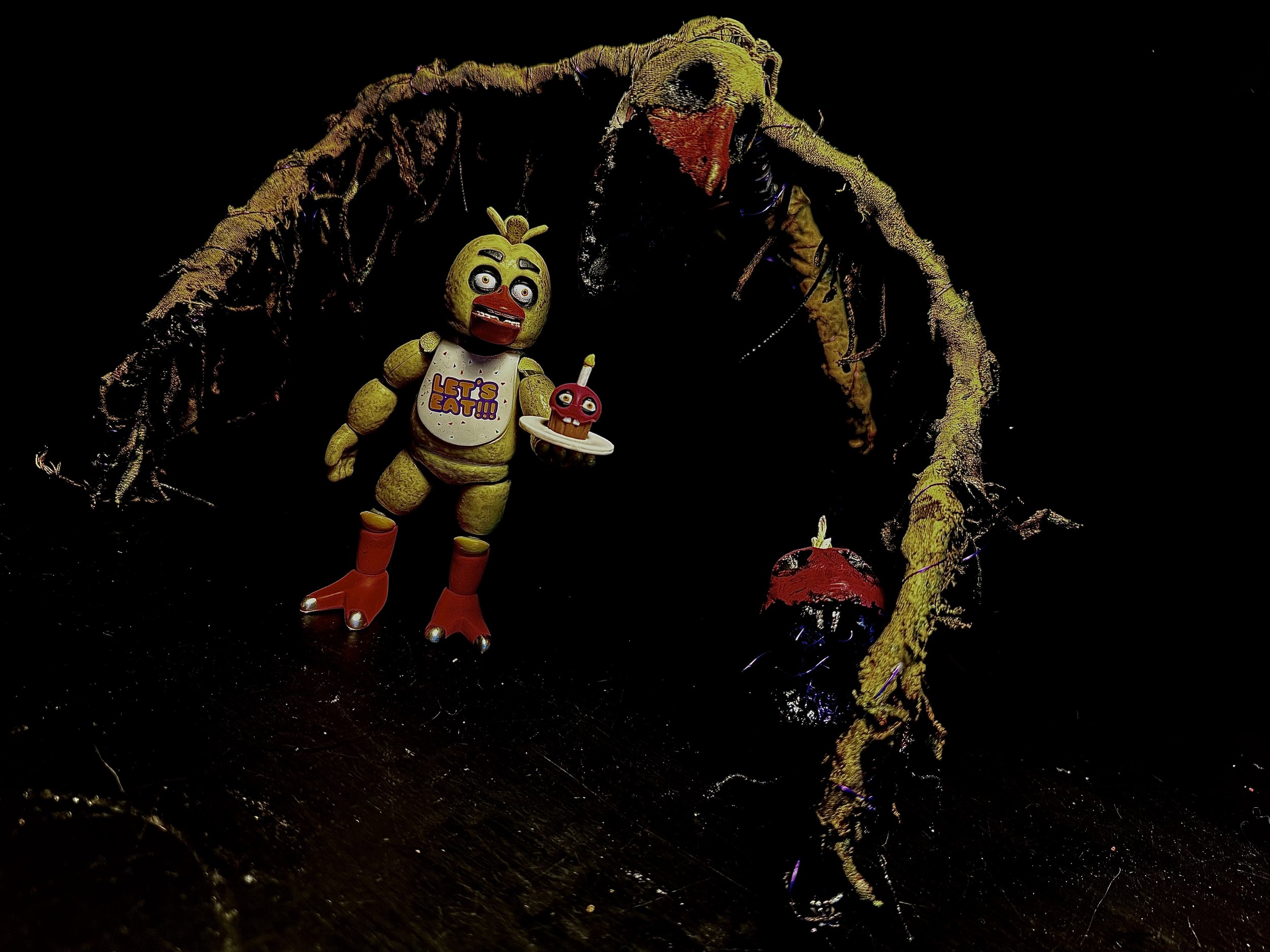A toy figure of an animatronic chick holding a cake, standing under a branch with a red mushroom. The chick is wearing red boots and a shirt with 'Let's Eat' written on it, and has a surprised facial expression with wide eyes and an open mouth.