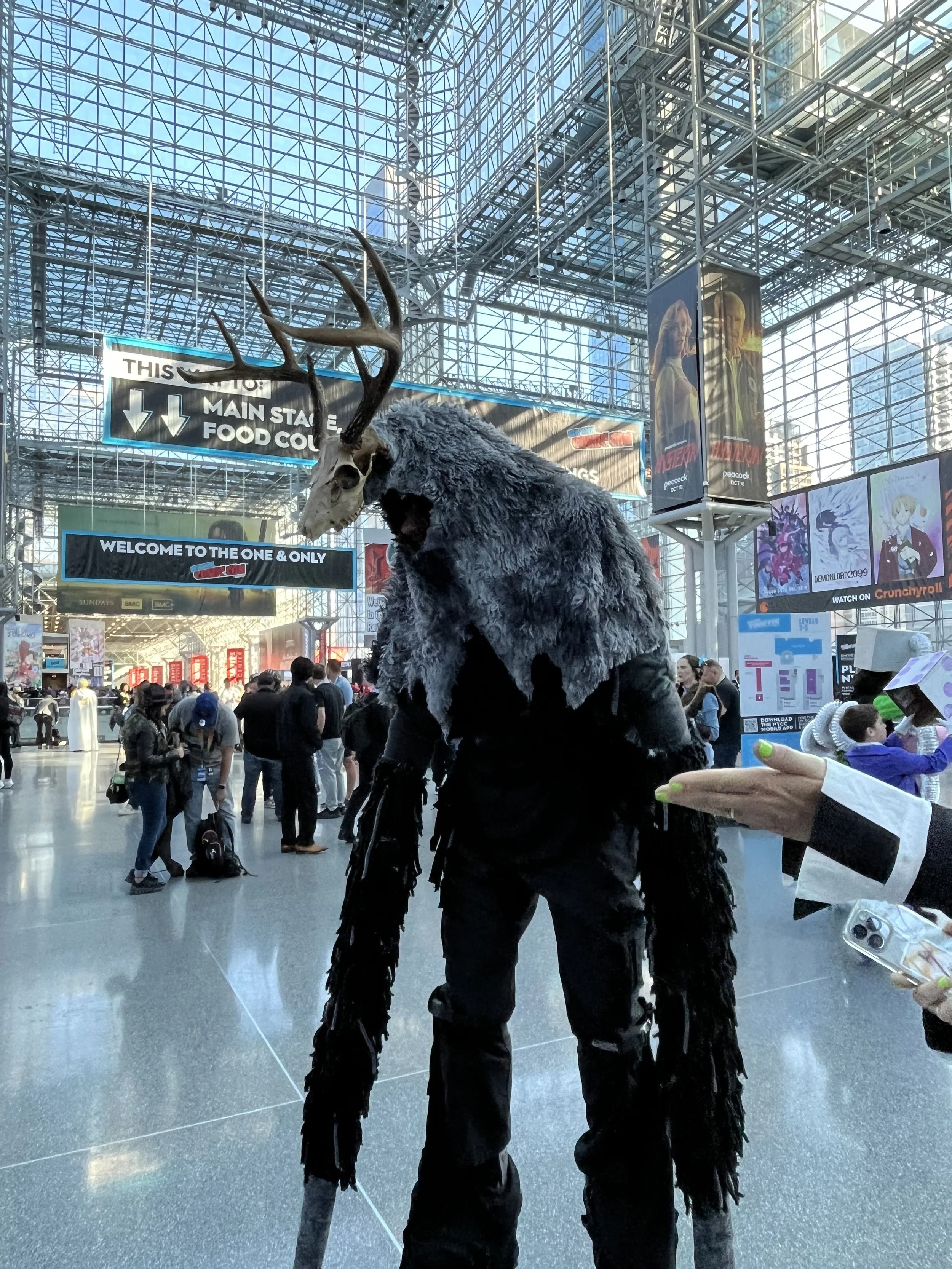A person dressed in a costume with a deer skull head and a furry coat at a busy convention center.