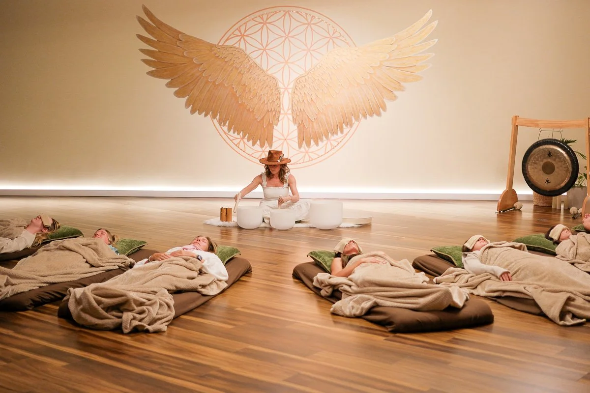 Modern building with large glass window set against mountainous landscape, surrounded by bushes.