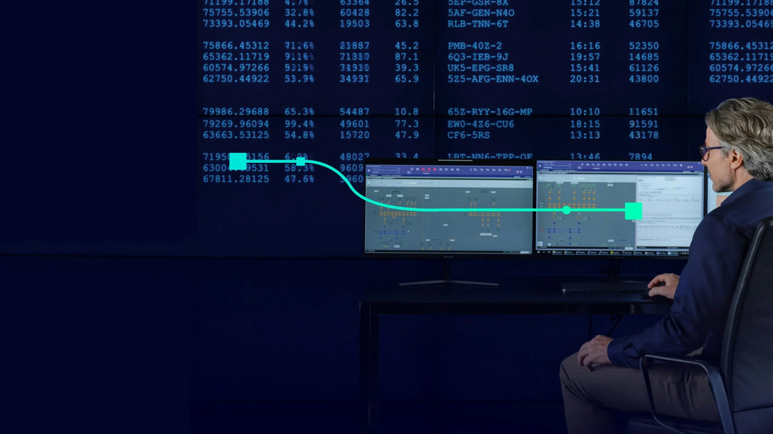 A man sitting at a desk with multiple monitors showing data charts and spreadsheets, in front of a large screen displaying blue numerical data, likely in a control center or trading room.