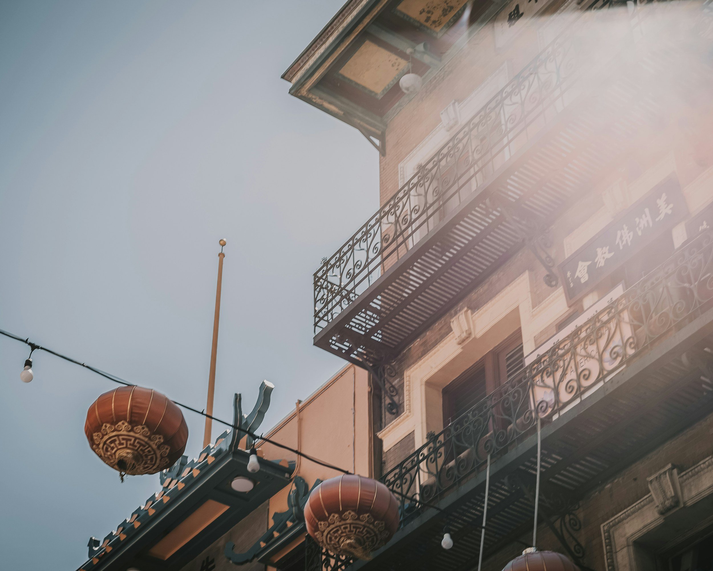Sunlight reflecting off a building with balconies, Chinese lanterns hanging outside, and string lights across the street
