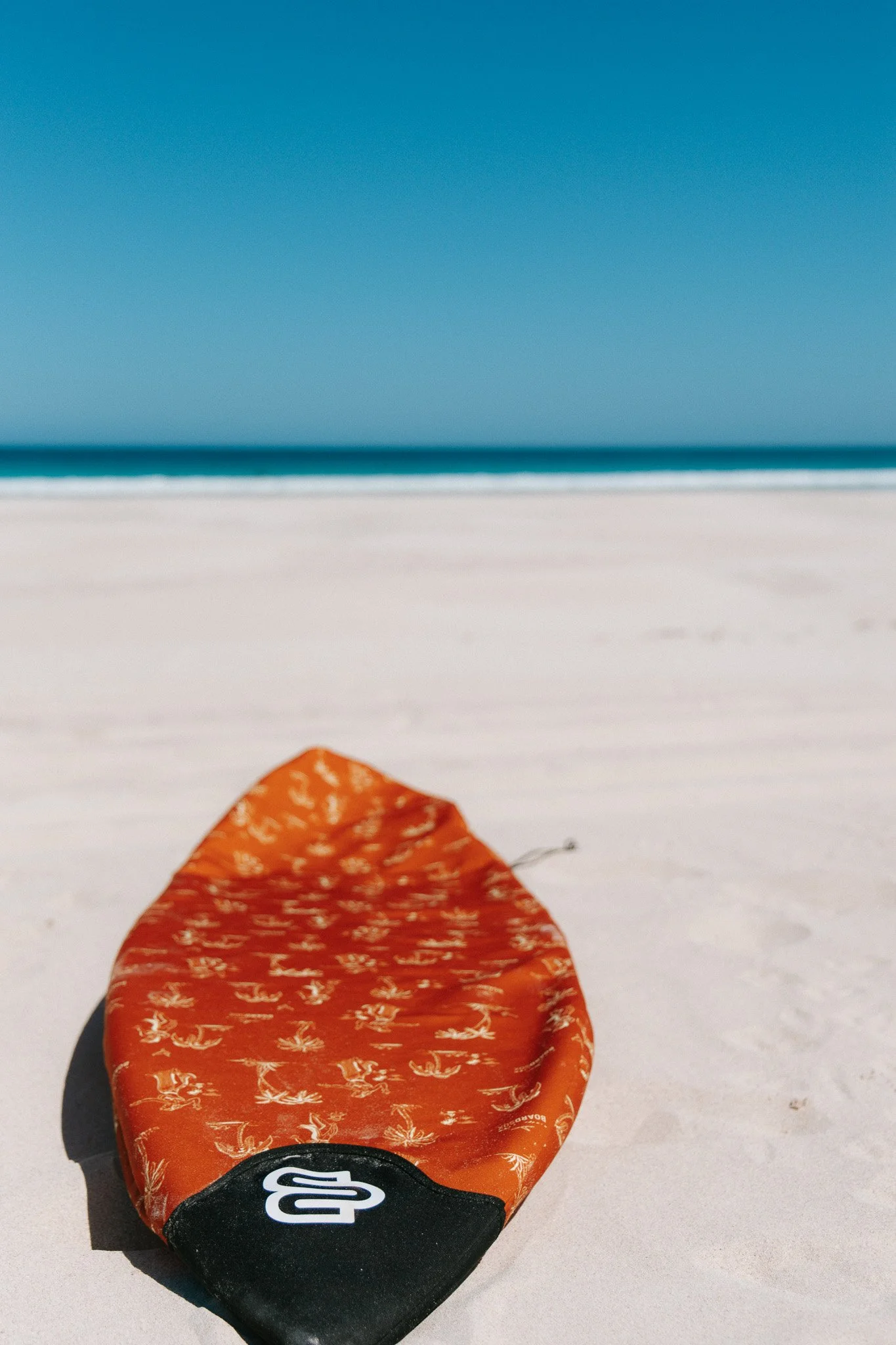 Close-up of an orange lifeguard float on a sandy beach with calm ocean and blue sky in the background.