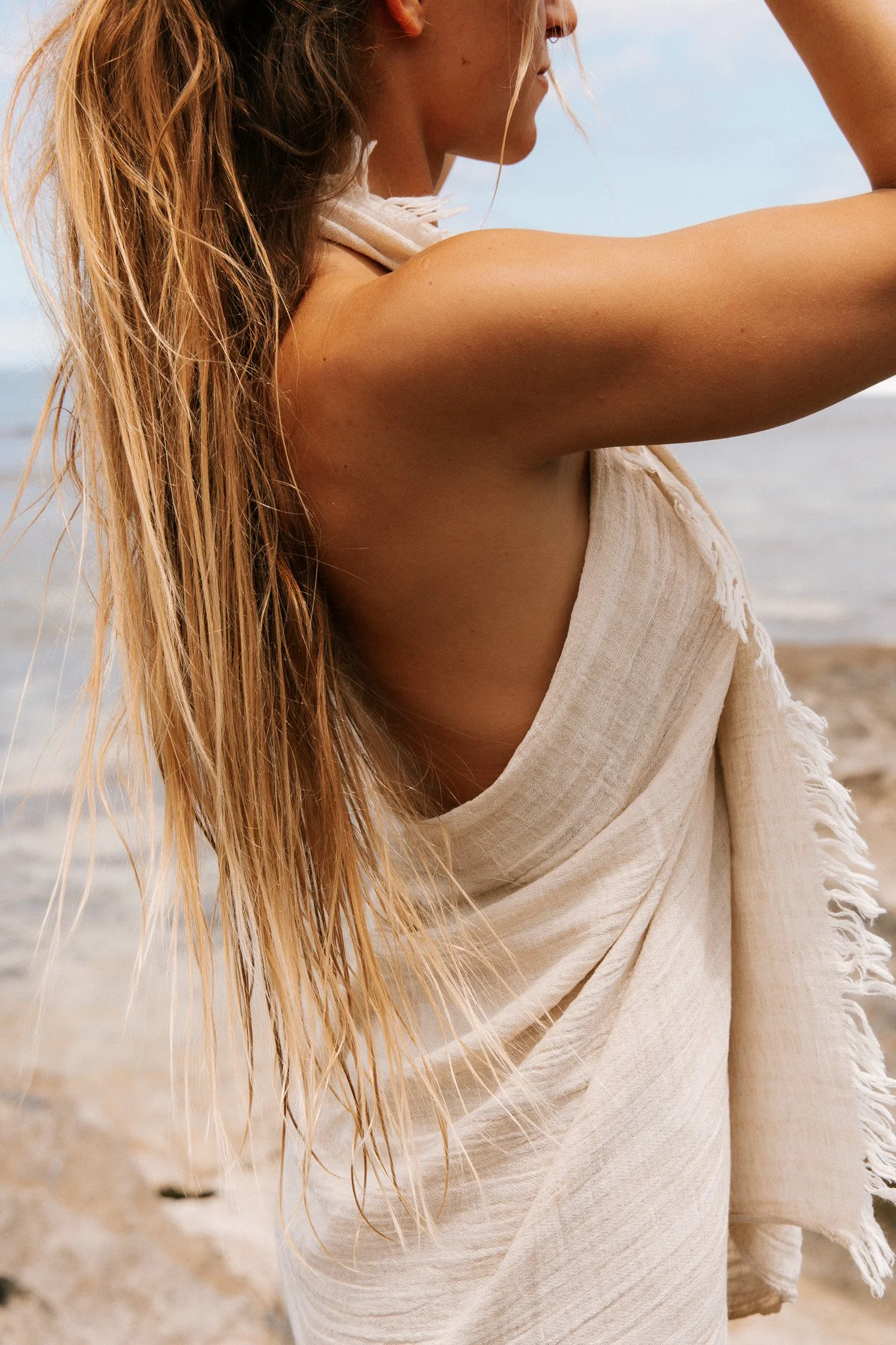 A woman with long blonde hair on a beach, wearing a sarong.