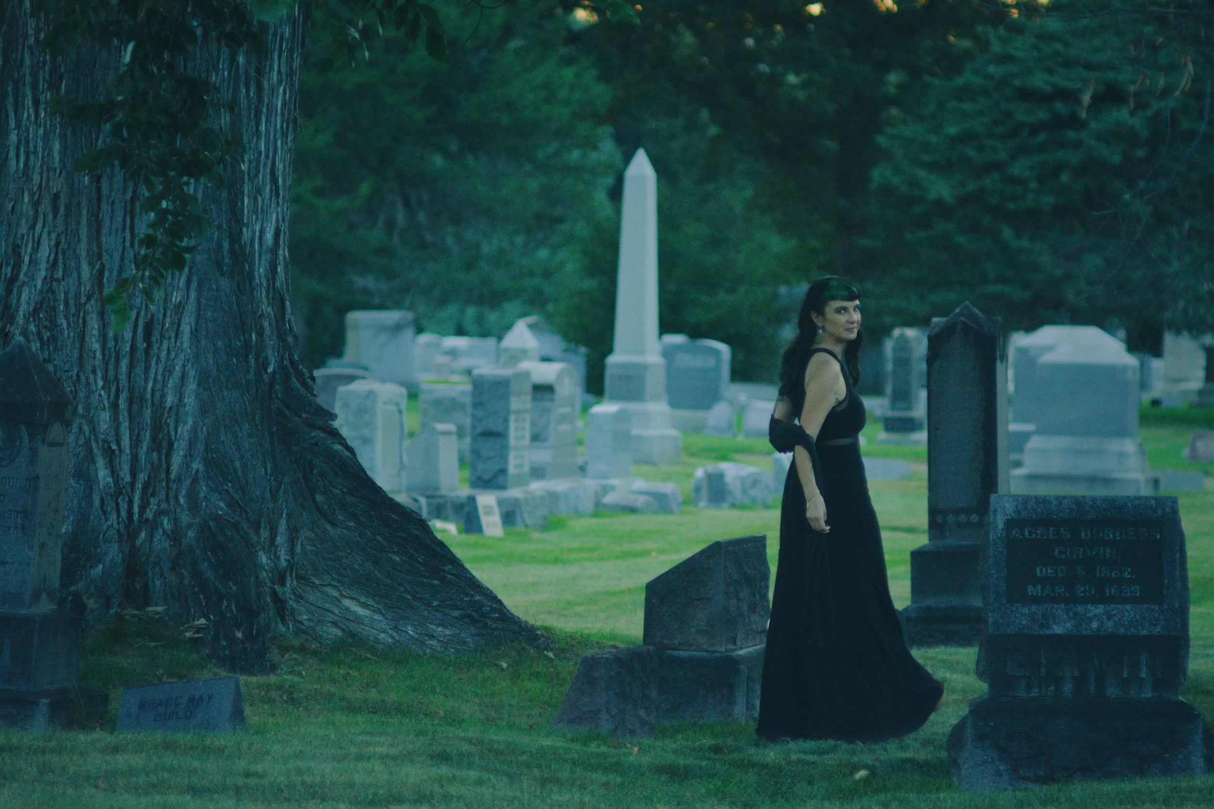 Wandering through the tombstones at a distance, looking over her shoulder to smile at the camera.
