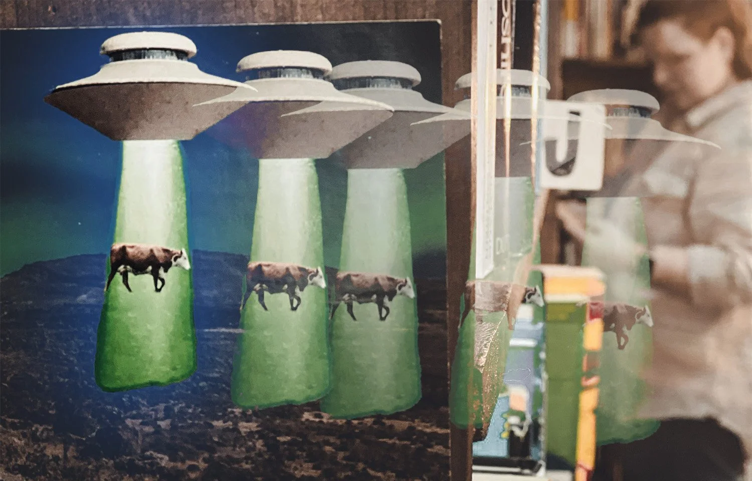The image of a UFO abducting a cow jumps off a book cover and floats into the aisle, where Brianne stands in the background.
