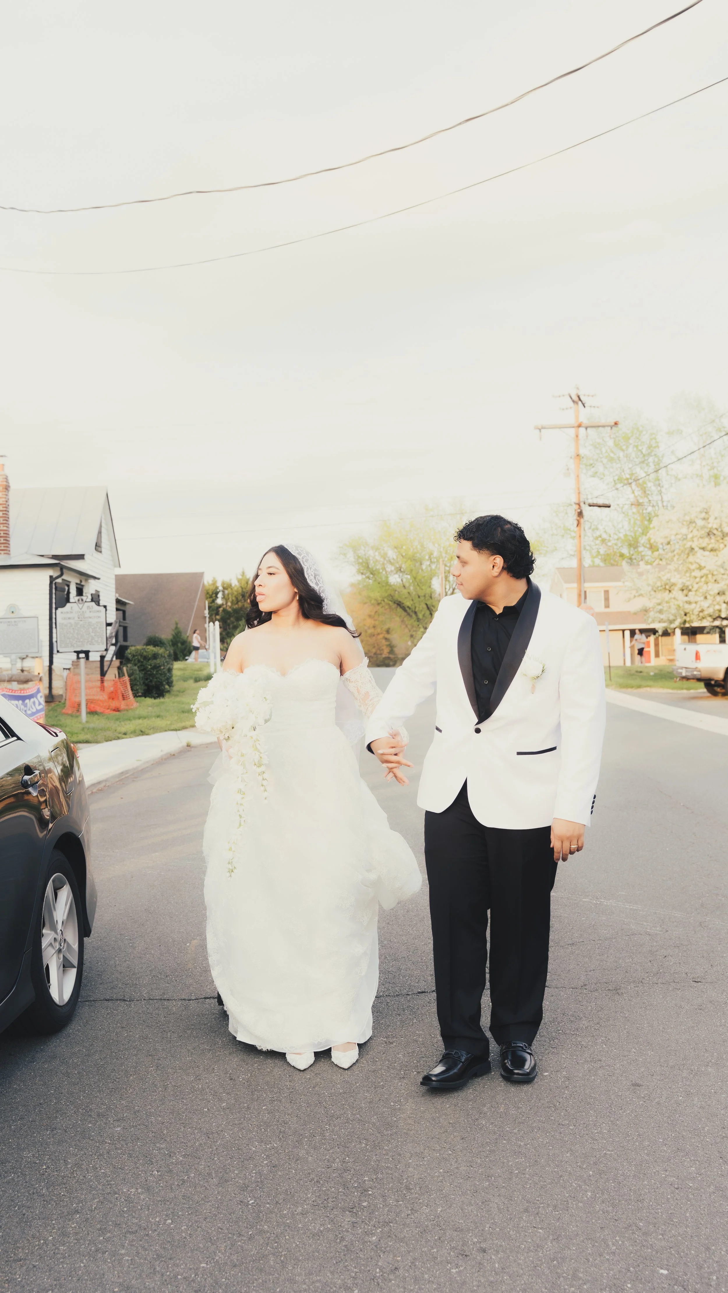 A bride and groom walking hand in hand on a street.