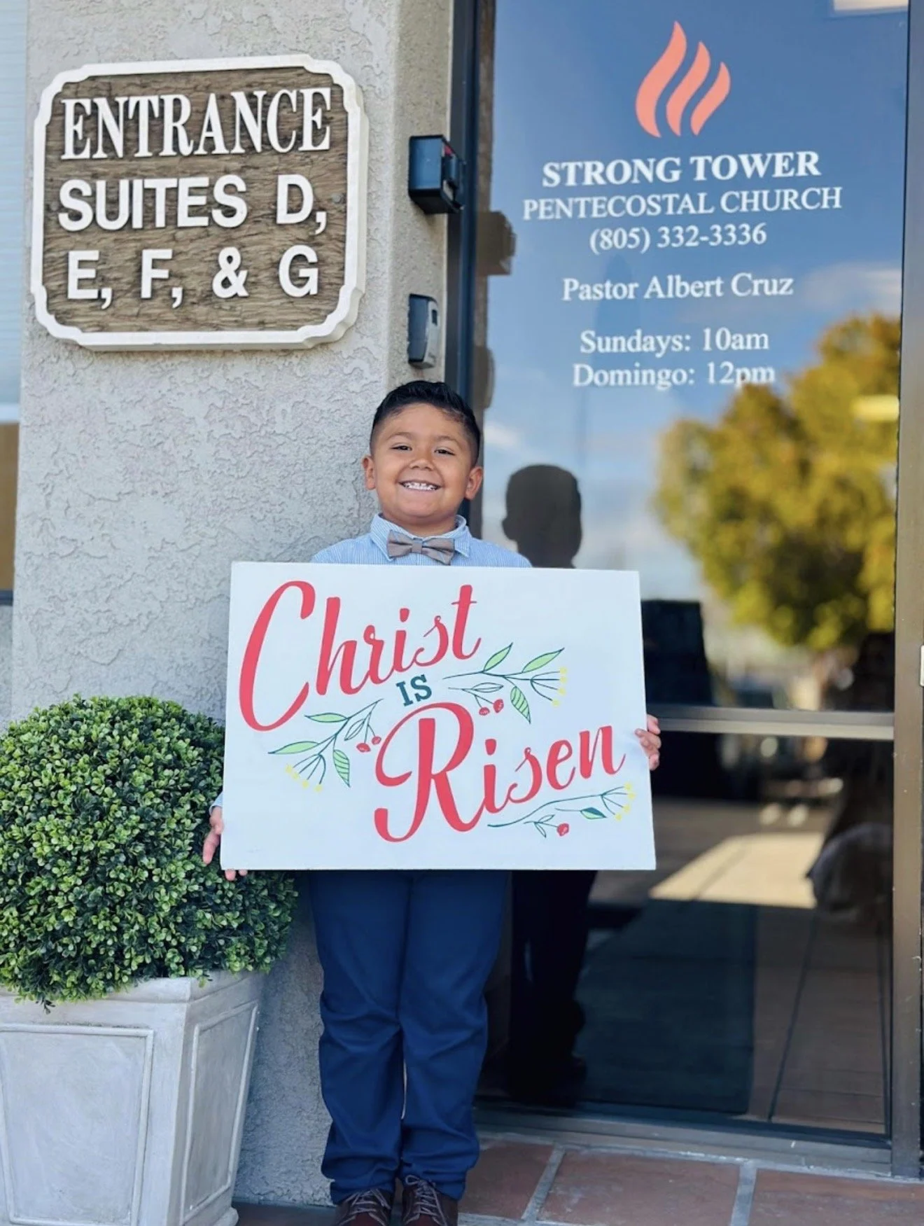 Child smiling with a welcome sign in front of Strong Tower Pentecostal Church in Santa Maria, CA