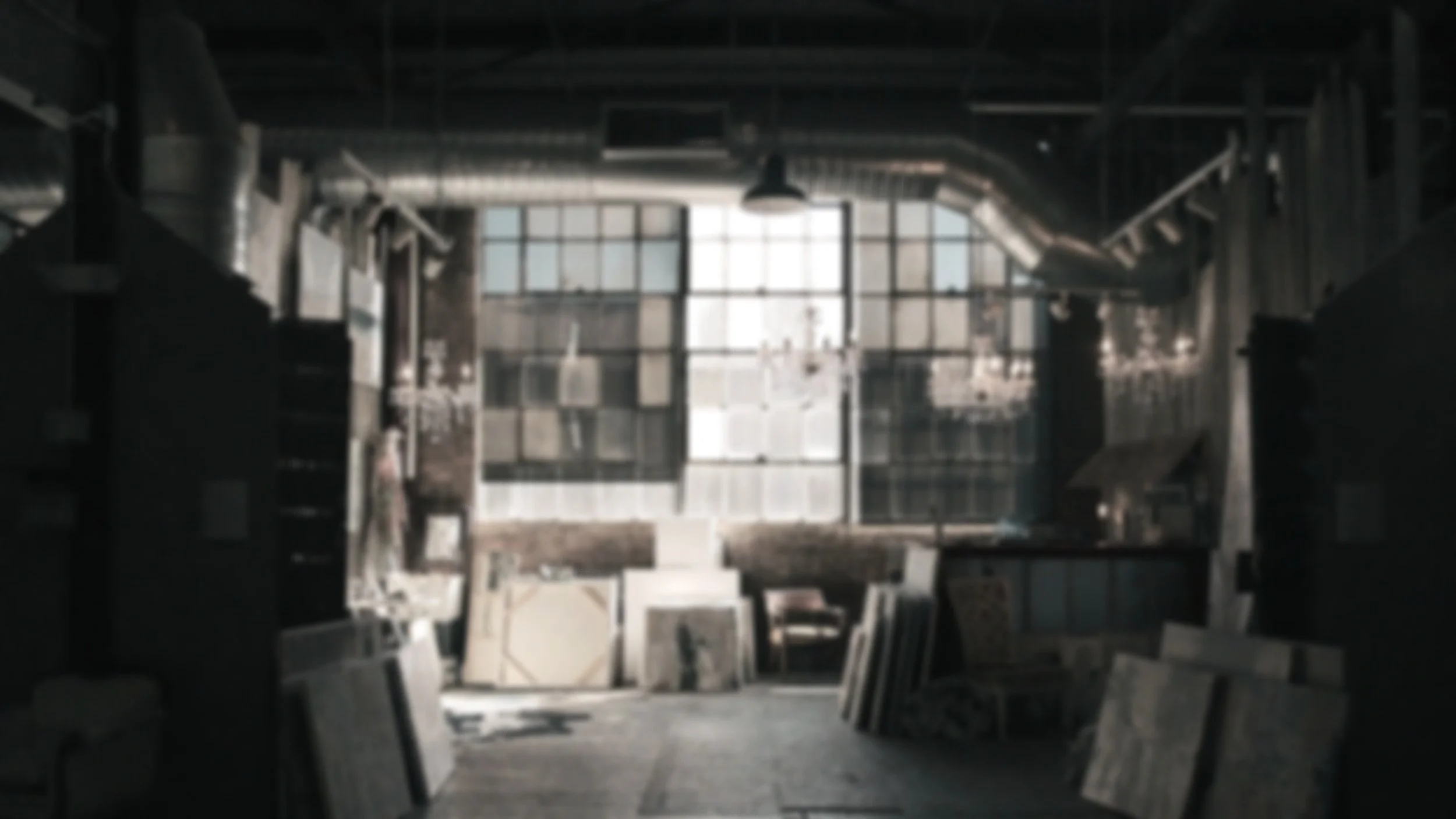 Interior of an old art studio or gallery with large windows, shelves with art supplies, and various artworks and canvases stacked against the walls.