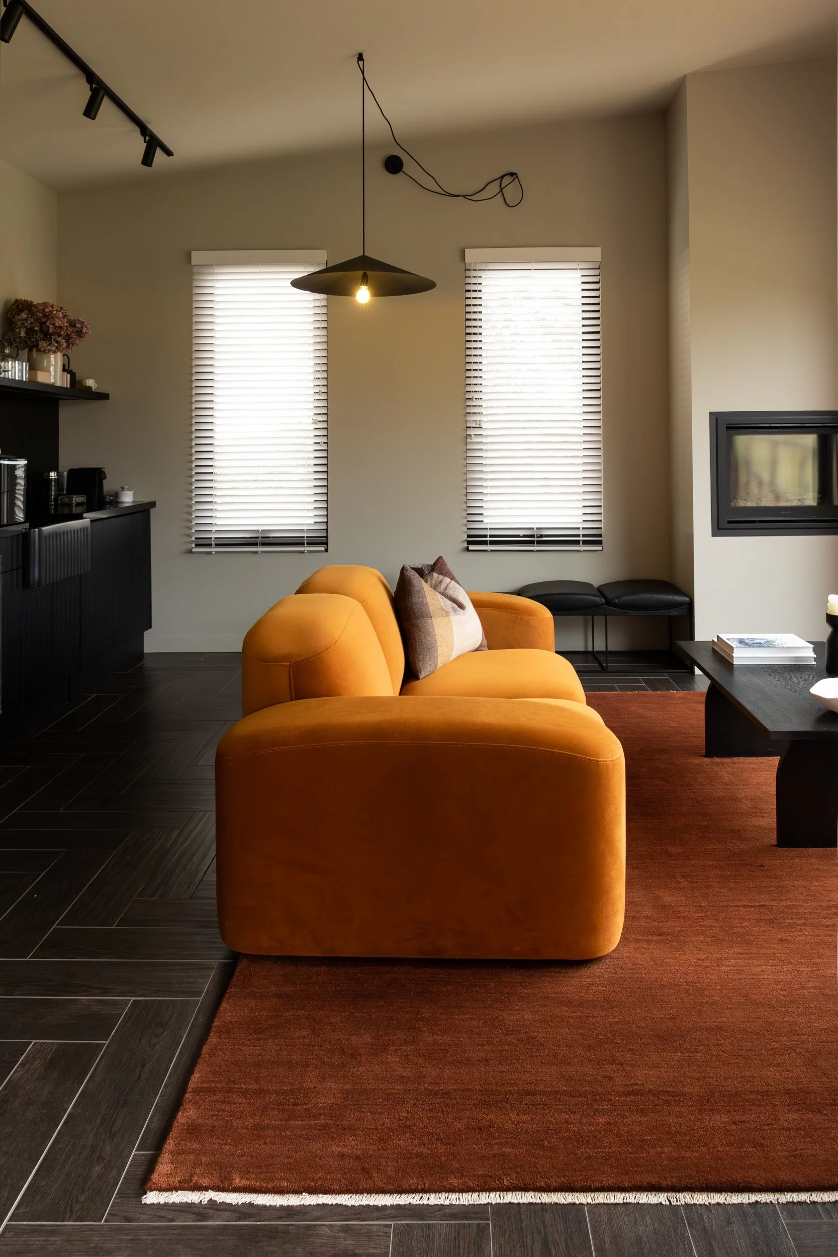 Living area at Carlton River Airbnb with a curved mustard sofa, terracotta rug and black kitchenette
