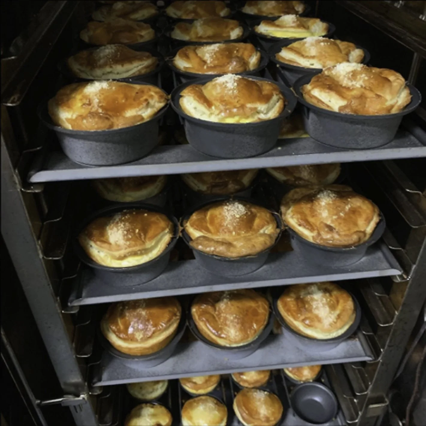 Multiple trays of baked pies, in a commercial oven.