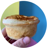 A hand holding a small pie with a golden-brown crust against a colorful background.