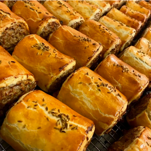 Several freshly baked meat pies with golden-brown crusts, garnished with herbs on a cooling rack.