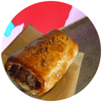 A baked pork & fennel sausage roll on a paper-lined tray with a red background.