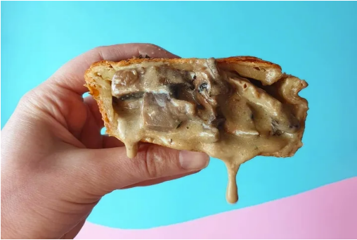 Slice of creamy mushroom pie held in hand against pastel blue and pink background.