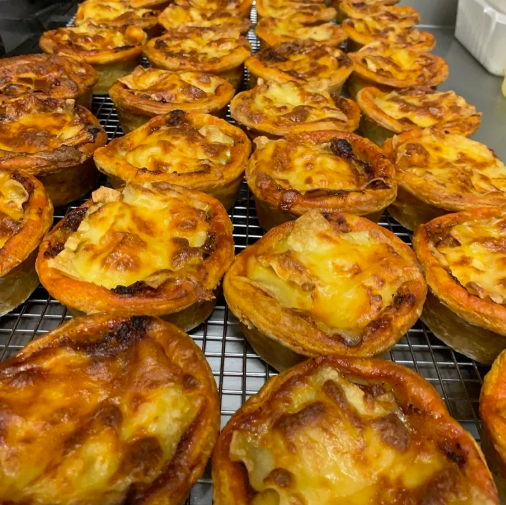 Several freshly baked mini quiches with melted cheese and bacon on top, cooling on a wire rack.