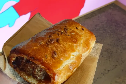 A baked pork & fennel sausage roll on a paper-lined tray with a red background.