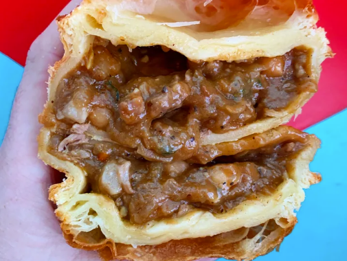 Close-up of a hand holding a flaky chunky steak pie