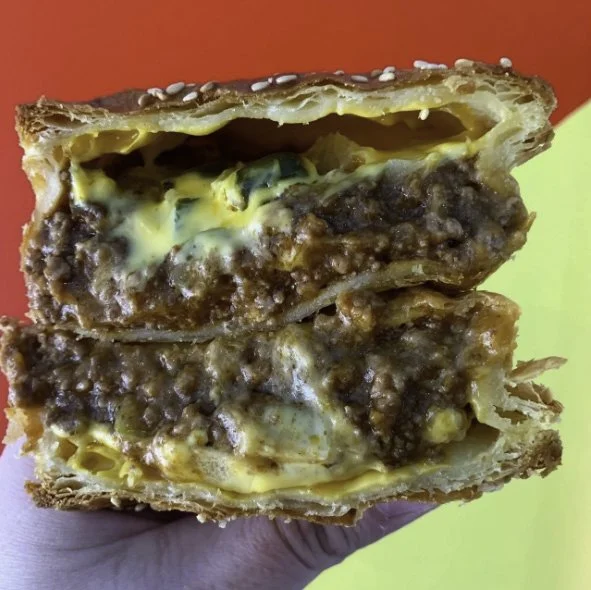Close-up of a cross-section of a beef and cheese pastry with sesame seeds on top, showing layers of pastry, meat, and melted cheese.