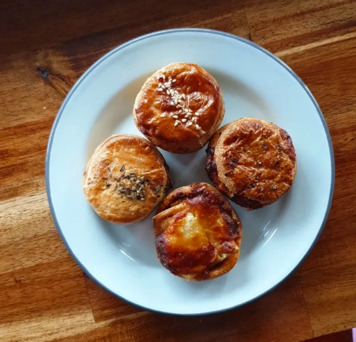 Four baked muffins on a white plate with a blue rim, placed on a wooden surface.