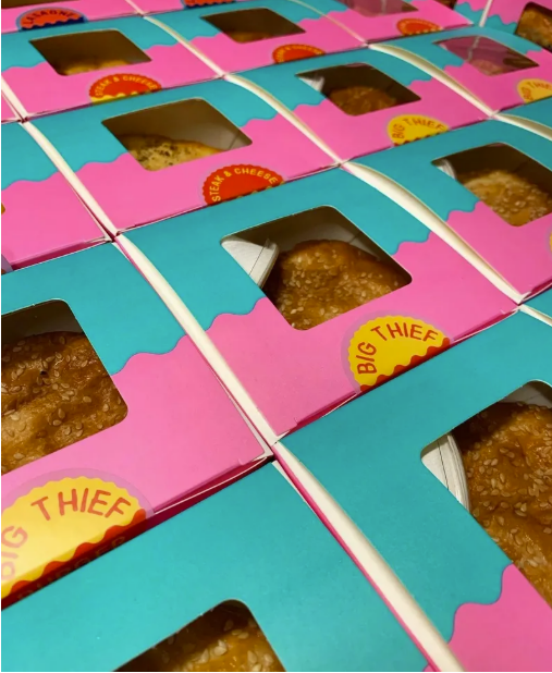 Multiple boxes of cookies with pink and blue packaging, labeled 'Big Thief,' with visible cookies through the window.
