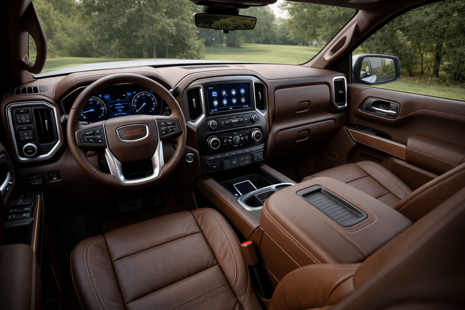 Interior of a GMC truck with a brown leather dashboard, steering wheel, and seats. The dashboard features a digital display, central touchscreen, and various control buttons. Outside view through the windshield shows a grassy area with trees.