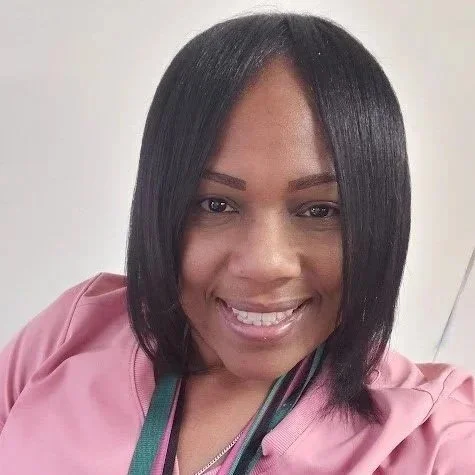 Portrait of a woman with straight black hair, smiling, wearing a pink top, and a lanyard around her neck.
