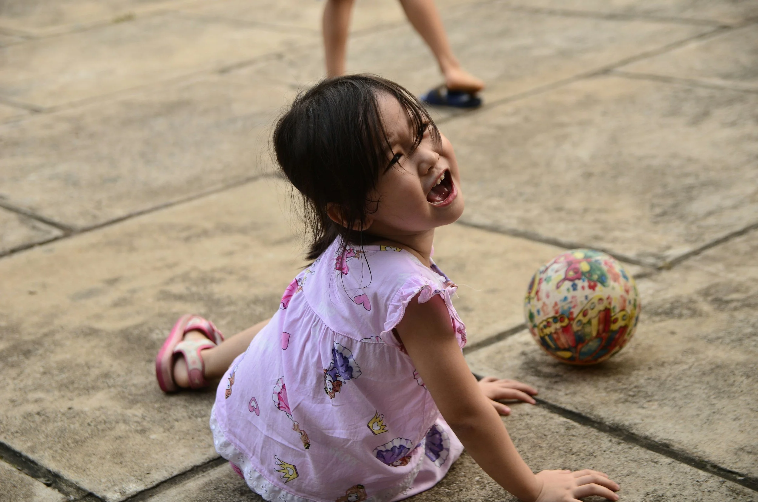 Young child sitting on ground playing with a ball, representing emotional expression and early signs of children’s mental health.