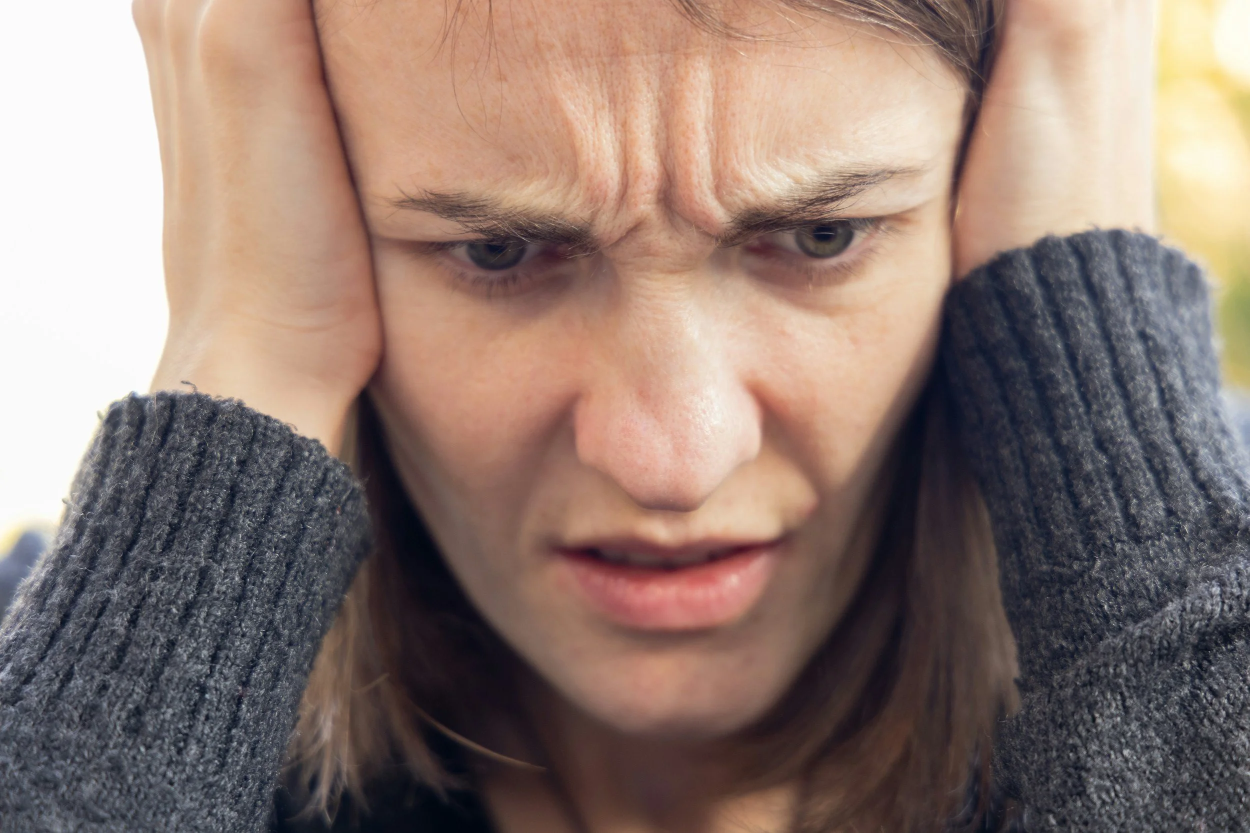 Woman holding her head with a distressed expression, representing emotional overwhelm, anxiety, and trauma-related stress responses.