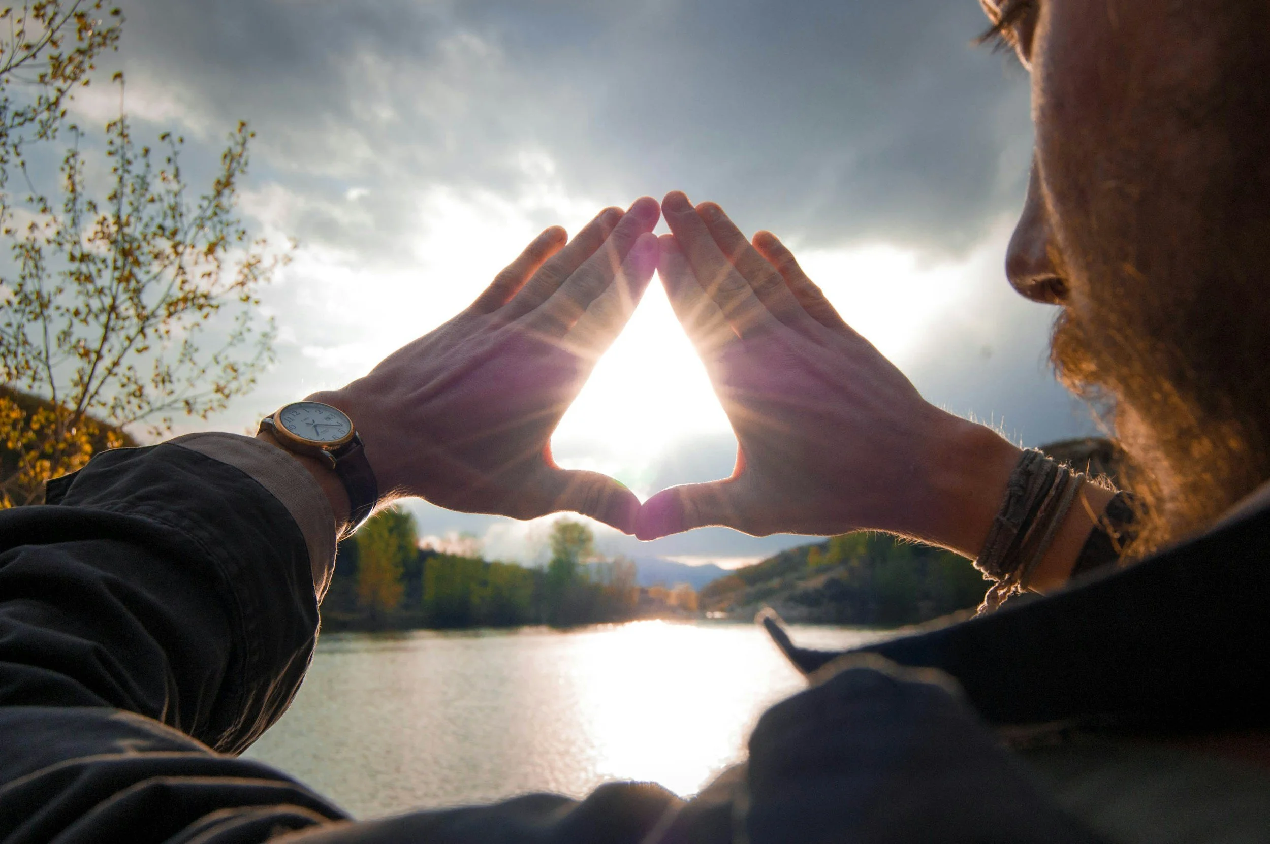 Person creating a heart shape with their hands while looking toward the sunlight, symbolizing self-love, emotional wellness, and healthy boundaries.