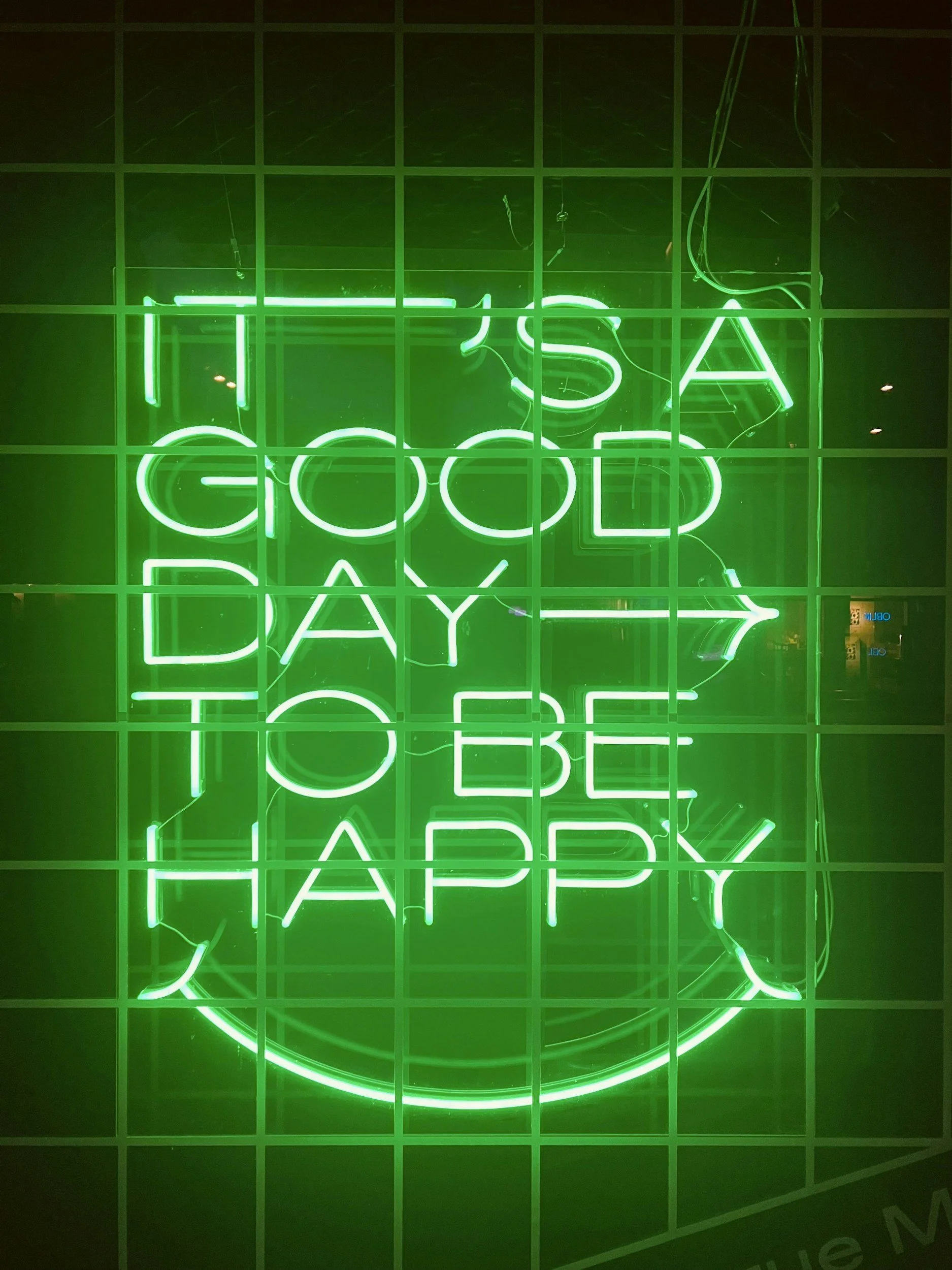 Green neon sign displaying the words "It's a Good Day to Be Happy," representing positive mindset and emotional balance.