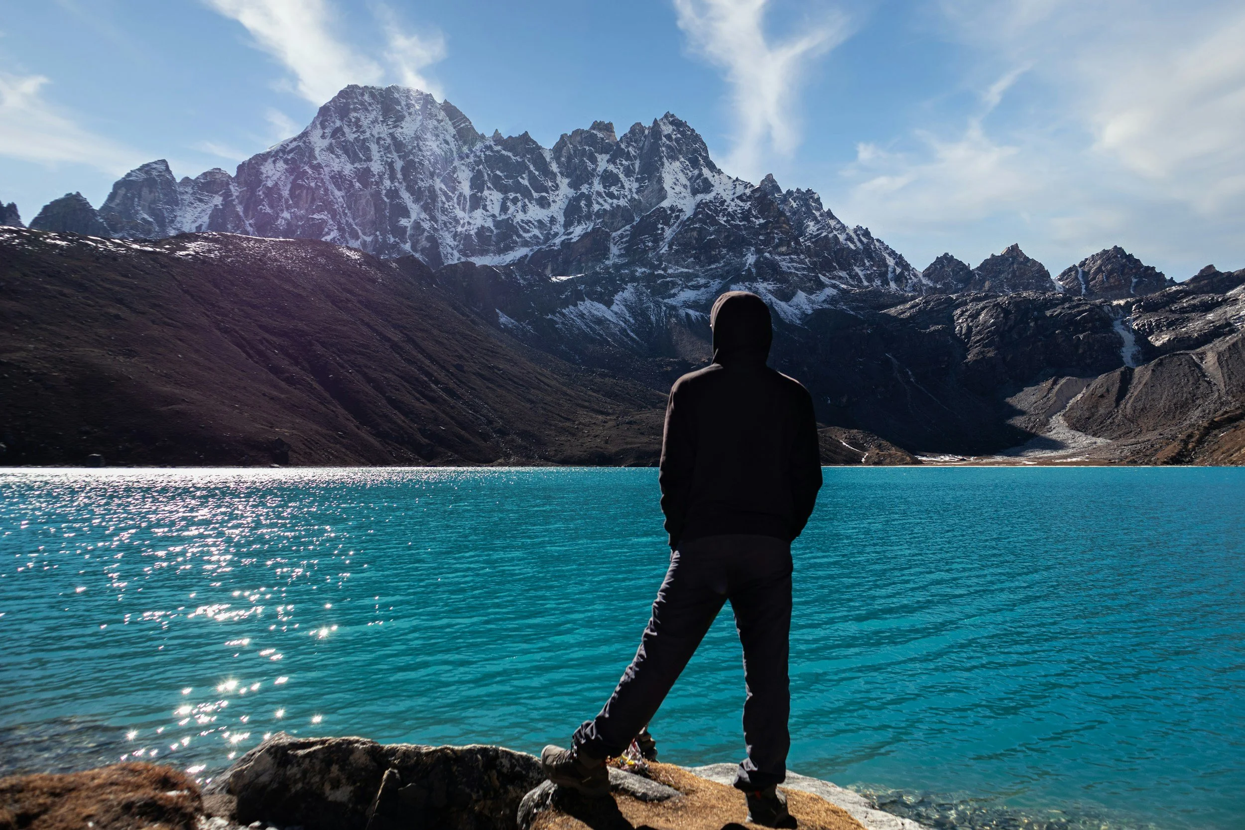 Person standing beside a crystal-blue lack with majestic mountains in the background, symbolizing hope, healing, emotional growth, and peace.