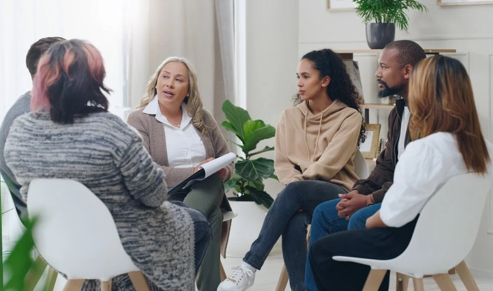 A group therapy session with five diverse people sitting in a circle and talking.