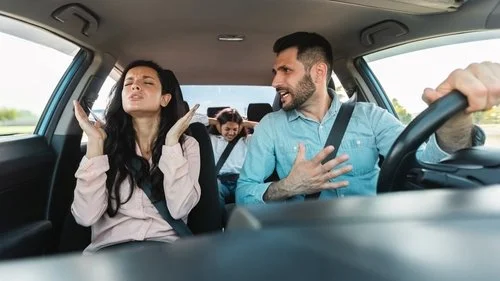 A man arguing while driving his wife and child in the car. The expression on their faces are irritated.