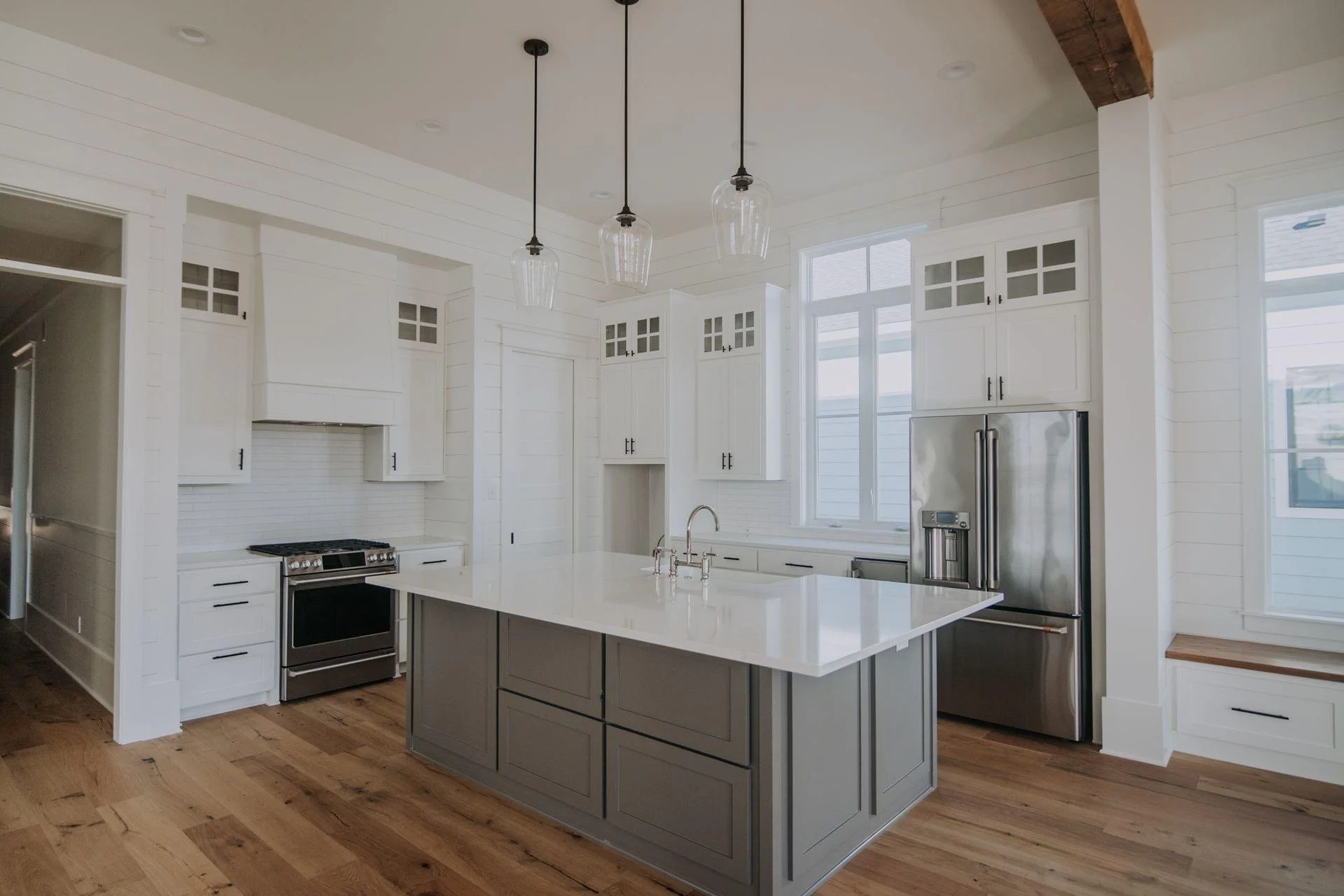 Modern white kitchen with an island, stainless steel fridge, oven, and three pendant lights hanging from the ceiling.