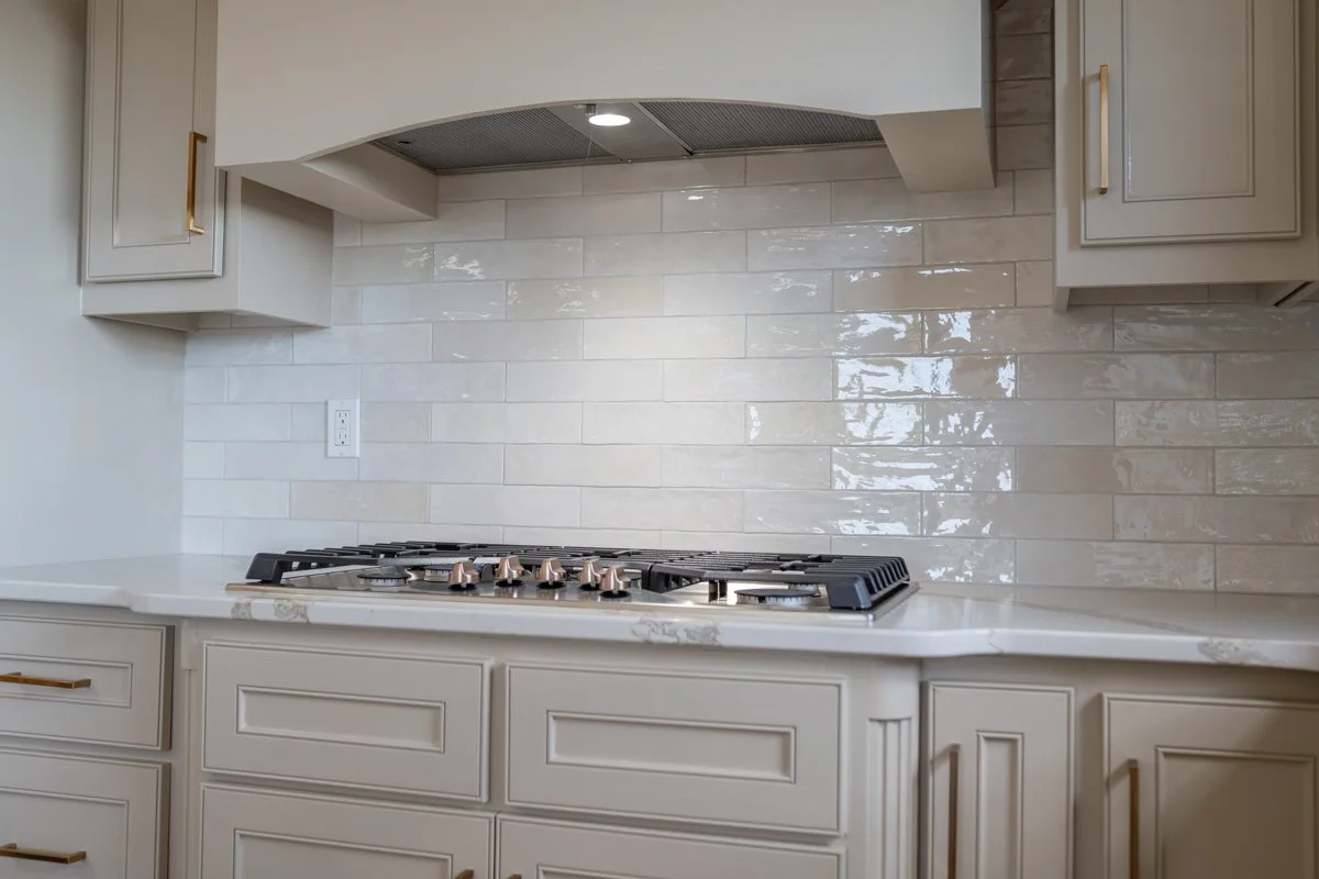 Kitchen with beige cabinets, white marble countertop, satin nickel hardware, beige tile backsplash, and a built-in gas stove with four burners.