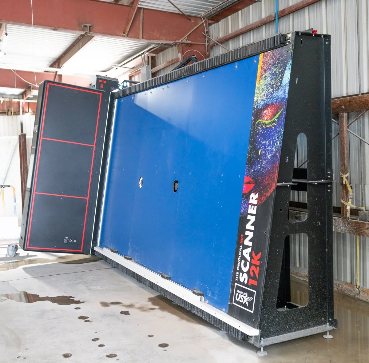 A large blue and black professional ping pong table with a colorful artistic face design on the side, located inside a warehouse building.
